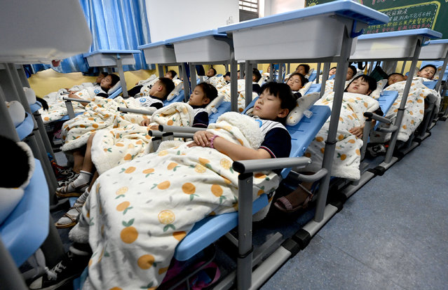 Students sleep in their foldable chairs under the lifted desks at a primary school in Handan in Hebei province Monday, June 13, 2022. The desk-chair set fit for the limited space in the classroom is a new invention with health benefits. Before that, students had to bend their necks to rest their heads on the desks during the compulsory noon nap time. (Photo credit should read HAO QY/ Feature China/Future Publishing via Getty Images)