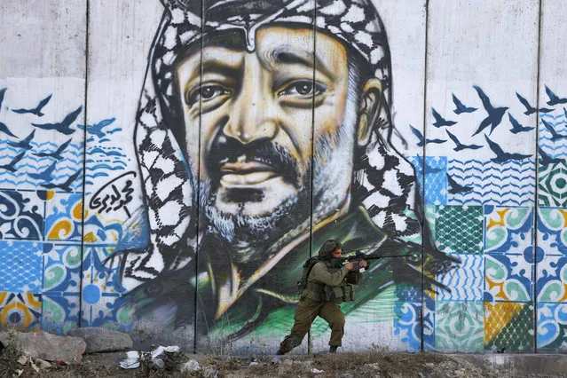 A member of the Israeli border guards looks through the scope of an assault rifle as he stands by a mural showing a graffiti image of late Palestinian leader Yasser Arafat, at the Qalandiya checkpoint near the West Bank city of Ramallah on July 19, 2017, during clashes after a protest by Palestinian youths against new Israeli security measures at the Al-Aqsa mosque compound, which include metal detectors and cameras, following an attack that killed two Israeli policemen. (Photo by Abbas Momani/AFP Photo)