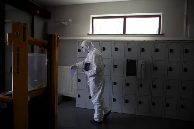 A worker in protective gear carries an urn of ashes of a Covid-19 deceased at the Pontes crematorium and funeral center in Wilrijk, Belgium, Friday, April 3, 2020. At the Wilrijk crematorium, near Antwerp, an extra 200 cremations due to Covid-19 have been done since the start of the week. (Photo by Virginia Mayo/AP Photo)