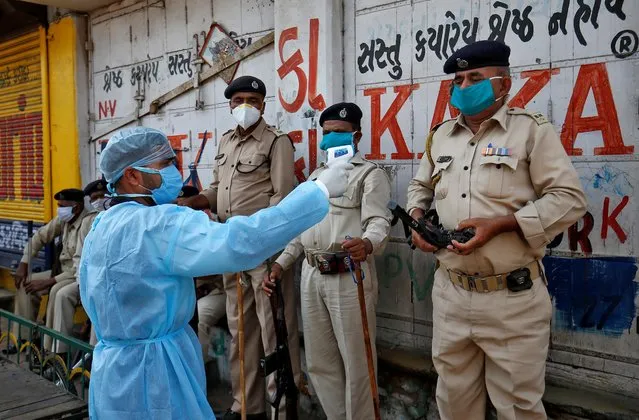 A paramedic uses an infrared thermometer to measure the temperature of a police officer alongside a road during a 21-day nationwide lockdown to slow the spreading of coronavirus disease (COVID-19) in Ahmedabad, India, April 9, 2020. (Photo by Amit Dave/Reuters)