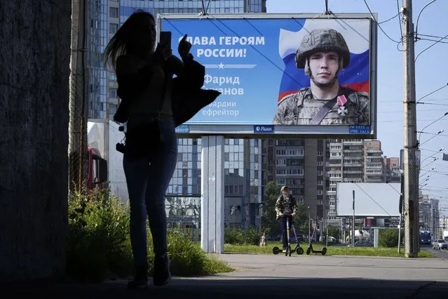 A woman uses her mobile phone as she walks past a billboard with a portrait of a Russian soldier and the words “Glory to the heroes of Russia” in St. Petersburg, Russia, Saturday, August 20, 2022. (Photo by Dmitri Lovetsky/AP Photo)