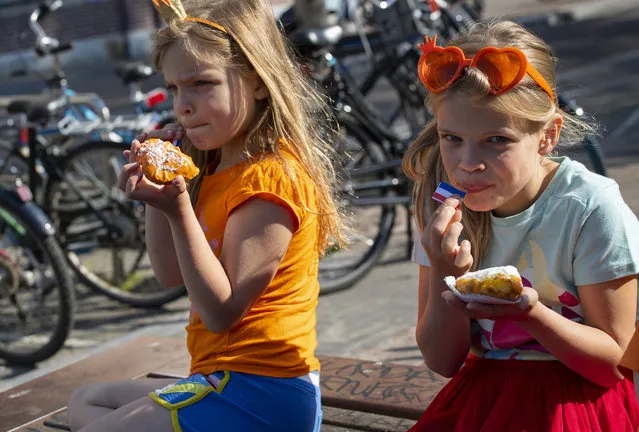 Two girls enjoy traditional King's Day pastry in Amsterdam, Netherlands, Monday, April 27, 2020. The Dutch national birthday party was a muted affair, dubbed King's Day at Home because of coronavirus restrictions, a far cry from the usual nationwide celebration with street parties. (Photo by Peter Dejong/AP Photo)