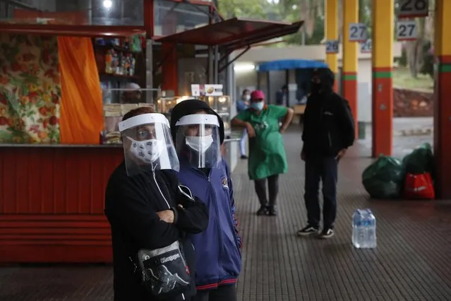 Passengers wearing face shields wait to take a bus at at the main bus station in Asuncion, Paraguay, Tuesday, May 12, 2020. The government is allowing bus travel up 100 km (about 62 miles) from the capital amid a partial lockdown amid the new coronavirus pandemic. (Photo by Jorge Saenz/AP Photo)
