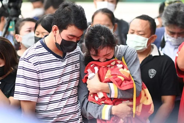 Sittipong Taothawong (L) comforts his wife Kanjana Buakumchan as she holds their child's milk bottle and blanket while standing outside the nursery in Na Klang in Thailand's northeastern Nong Bua Lam Phu province on October 7, 2022, the day after a former police officer killed at least 37 people in a mass shooting at the site. - Weeping, grief-stricken families gathered on October 7 outside a Thai nursery where an ex-policeman murdered nearly two dozen children in one of the kingdom's worst mass killings. (Photo by Manan Vatsyayana/AFP Photo)