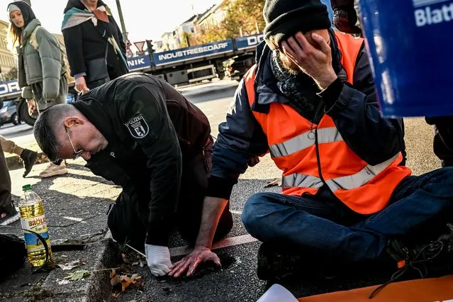 A police officer uses a brush and rapeseed oil as solvent to free a Letzte Generation (Last Generation) climate activist who glued his own hand to the asphalt as part of a protest roadblock in Berlin, Germany, 07 November 2022. Letzte Generation activists have been criticized by Germany's Green Party after one of their recent protests disrupted traffic, which may have prevented emergency services from reaching in time a road accident victim who later died. (Photo by Filip Singer/EPA/EFE/Rex Features/Shutterstock)