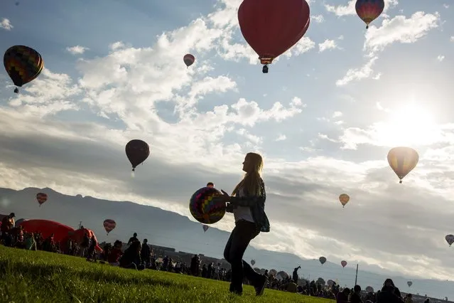 A woman carries a toy hot air balloon across a field as hundreds of hot air balloons lift off on the first day of the 2015 Albuquerque International Balloon Fiesta in Albuquerque, New Mexico, October 3, 2015. (Photo by Lucas Jackson/Reuters)