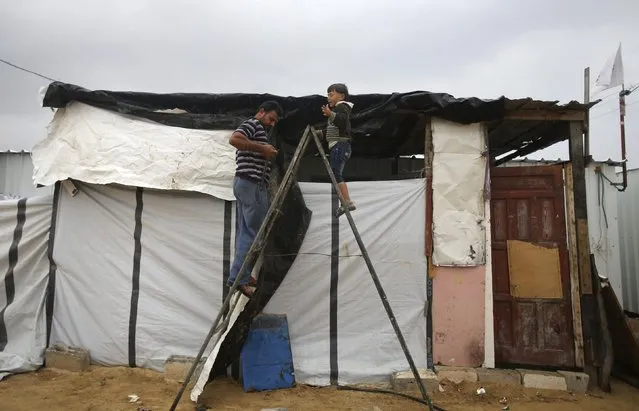 A Palestinian man, who lives in a container as a temporary replacement for his house that witnesses said was destroyed by Israeli shelling during the most recent conflict between Israel and Hamas, repairs the shelter on a rainy day in the east of Khan Younis in the southern Gaza Strip November 16, 2014. (Photo by Ibraheem Abu Mustafa/Reuters)