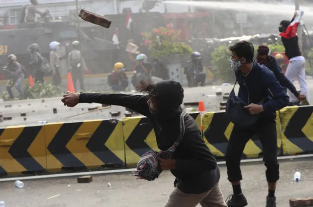 A protesters hurls a brick towards police trying to contain a rally in Jakarta, Indonesia, Thursday, October 8, 2020. (Photo by Achmad Ibrahim/AP Photo)