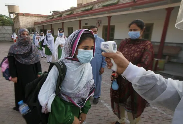 A worker checks body temperature of students upon her arrival at a school in Peshawar, Pakistan, Wednesday, September 23, 2020. Pakistani officials welcomed millions of students back to middle schools following educational institutions reopened in the country amid a steady decline in coronavirus deaths and infections. (Photo by Muhammad Sajjad/AP Photo)