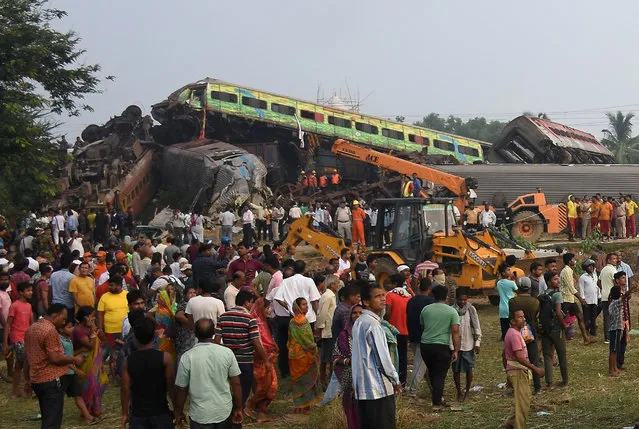 People stand next to damaged coaches after two passenger trains collided in Balasore district in the eastern state of Odisha, India on June 3, 2023. (Photo by Reuters/Stringer)
