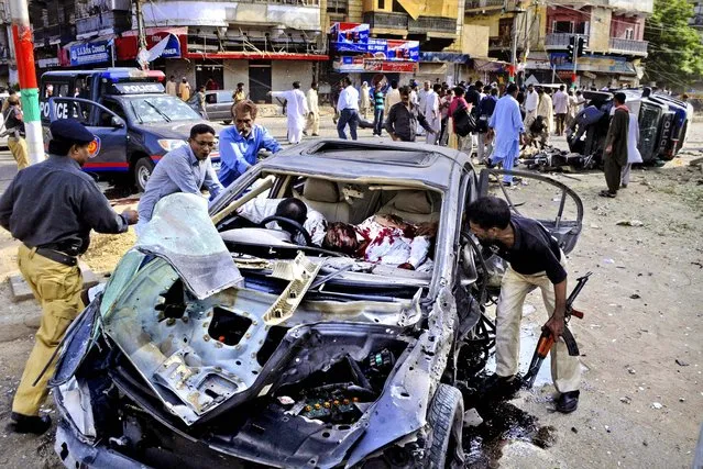 Police officers and civilians move the lifeless bodies of a driver and a policeman after a bomb blast in Karachi, Pakistan, on June 26, 2013. A bomb targeting a senior judge in Karachi wounded him and killed several security personnel. (Photo by Wasi Qureshi/Associated Press)