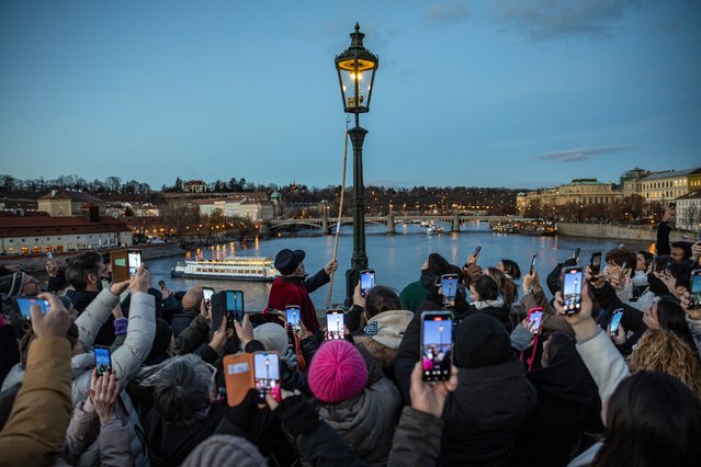 People hold up their smartphones as they watch lamplighter Jan Tater (C), wearing a 19th-century historical uniform, as he lights a historic gas lamp on Charles Bridge in Prague, Czech Republic, 17 December 2024. Every day at dusk during Advent, lamplighter Jan Tater and his colleague manually light the 46 historic gas lanterns along Prague's iconic Charles Bridge and its surroundings as an attraction for tourists. The first gas lamps in Prague were ceremonially lit in 1847. (Photo by Martin Divíšek/EPA/EFE)