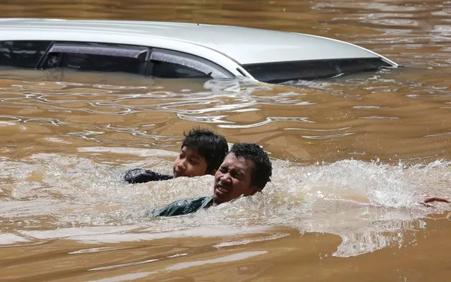 People swim through a flooded neighborhood following heavy rains in Jakarta, Indonesia, Saturday, February 20, 2021. Heavy downpours combined with poor city sewage planning often causes heavy flooding in parts of greater Jakarta. (Photo by Tatan Syuflana/AP Photo)