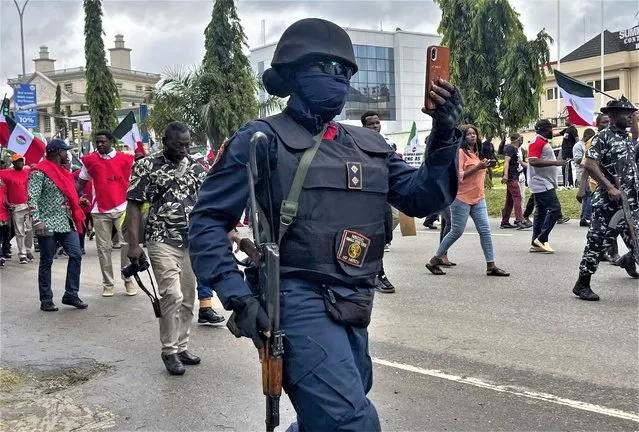 A nigerian police officer takes photographs of labour unionists marching in the streets of Abuja, Nigeria, Wednesday, August 2, 2023, to protest the soaring cost of living under the West African nation's new president, with calls for the government to improve social welfare interventions to reduce hardship. (Photo by Chinedu Asadu/AP Photo)