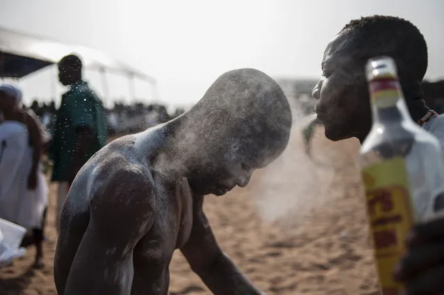 A voodoo devotee sprays gin over another to chase away bad spirits on a beach in Ouidah on January 10, 2016. Officially declared a religion in Benin in 1996, Voodoo and the Voodoo festival attracts thousands of devotees and tourists for a day filled with ritual dances, goat slaughtering and gin drinking. Benin's voodoo festival is held every year and is the West African country's most vibrant and colourful event. (Photo by Stefan Heunis/AFP Photo)