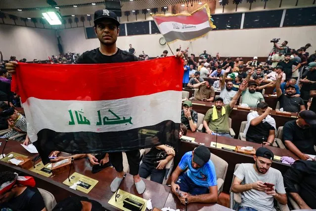 A man deploys a national flag as supporters of the Iraqi cleric Moqtada Sadr gather inside the country's parliament in the capital Baghdad's high-security Green Zone, to protest against a rival bloc's nomination for prime minister, on July 30, 2022. The protests are the latest challenge for oil-rich Iraq, which remains mired in a political and a socioeconomic crisis despite elevated global energy prices. Sadr's bloc emerged from elections in October as the biggest parliamentary faction, but was still far short of a majority and, nine months on, deadlock persists over the establishment of a new government. (Photo by Ahmad Al-Rubaye/AFP Photo)