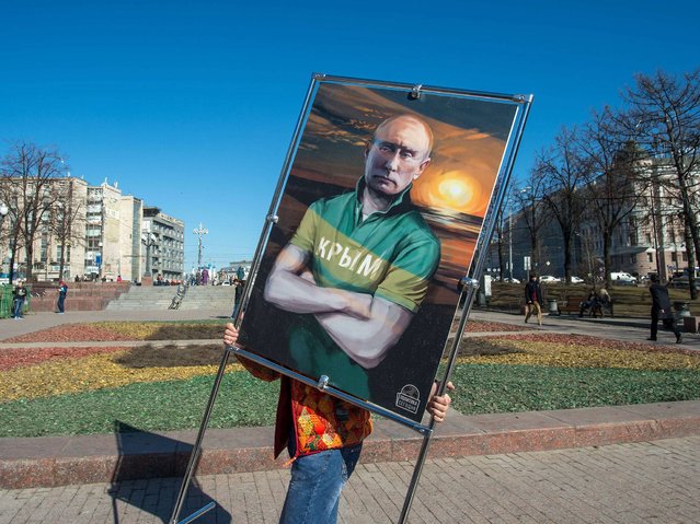 A man carries a picture depicting Russia's President Vladimir Putin in a T-shirt with an inscription reading: “Crimea” at an open-air political cartoons exhibition dedicated to the one-year anniversary of Crimea voting to leave Ukraine and join the Russian state in central Moscow on March 16, 2015. (Photo by Dmitry Serebryakov/AFP Photo)