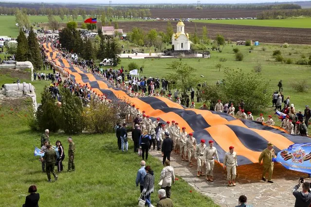Activists carry a 300 meter long St. George ribbon, which has become a symbol of the pro-Russian insurgency in eastern Ukraine, during celebrations of the Victory Day at a World War II memorial in Saur-Mogila, about 60 km. (31 miles) east of Donetsk, eastern Ukraine, Saturday, May 8, 2021. Efforts have stalled to end the conflict between Russia-backed rebels and Ukrainian forces, which has killed more than 14,000 people since it broke out in 2014. Russia, which claims it has no military presence in eastern Ukraine, fueled the tensions this year by massing troops and conducting large-scale military exercises near its border with Ukraine. (Photo by Alexei Alexandrov/AP Photo)