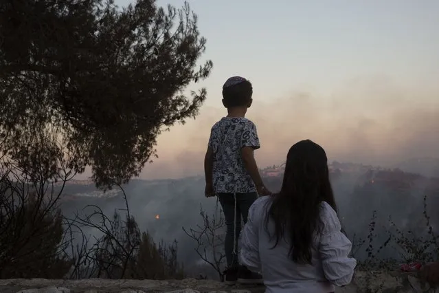 An Israeli mother and son watch from an overlook as firefighters battle wildfires for the second day near Shoresh, on the outskirts of Jerusalem, Monday, August 16, 2021. Israel Fire and Rescue service said in a statement that 45 firefighting teams accompanied by eight planes were working to contain five fires in the forested hills west of the city. (Photo by Maya Alleruzzo/AP Photo)