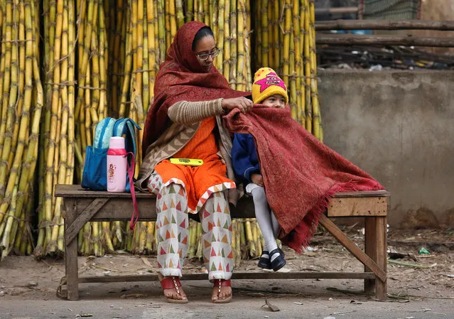 A mother covers her daughter with a stole to keep her warm as they wait for a school bus on a cold winter morning in Kolkata, January 18, 2019. (Photo by Rupak De Chowdhuri/Reuters)