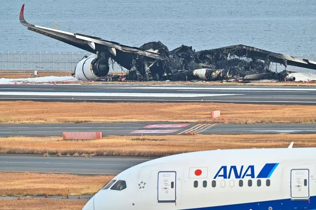 An All Nippon Airlines (ANA) plane taxis past the burnt wreckage of a Japan Airlines (JAL) passenger plane on the tarmac at Tokyo International Airport at Haneda in Tokyo on January 3, 2024, the morning after the JAL airliner hit a smaller coast guard plane on the ground. Five people aboard a Japan coast guard aircraft died on January 2 when it hit a Japan Airlines passenger plane on the ground in a fiery collision at Tokyo's Haneda airport. (Photo by Richard A. Brooks/AFP Photo)