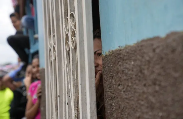 A woman looks through a wrought iron window during an event for kids at a soup kitchen in the neighborhood of Antimano in Caracas, Venezuela, Tuesday, July 27, 2021. The soup kitchen was celebrating a belated national Children's Day, amid the new coronavirus pandemic. (Photo by Ariana Cubillos/AP Photo)