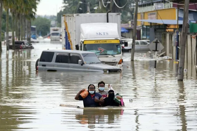 Residents wade through a flooded road in Shah Alam, on the outskirts of Kuala Lumpur, Malaysia, Monday, December 20, 2021. (Photo by Vincent Thian/AP Photo)