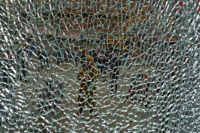 People are seen through a broken window of a shop in Srinagar on January 25, 2022, after suspected militants threw a hand grenade towards government forces. (Photo by Tauseef Mustafa/AFP Photo)