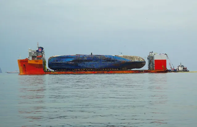 This handout photo provided and taken on March 26, 2017 by the South Korean Maritime Ministry shows the wreck of the Sewol ferry placed onto a submersible vessel off the coast of the southern South Korean island of Jindo. South Korea' s sunken Sewol ferry has been successfully hauled onto a giant heavy lifting ship, officials said on March 25, a step towards returning the vessel to port. (Photo by AFP Photo/South Korean Maritime Ministry)