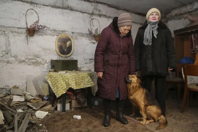 Liliya, left, and Tatyana, both residents of Donetsk-Severne village in the outskirts of Donetsk, speak to a journalist in a basement used as a bomb shelter on the territory controlled by pro-Russian militants not far from the frontline with Ukrainian government forces, eastern Ukraine, Sunday, January 30, 2022. Liliya and five other people live in a five-storey apartment building without heating and water supply. Many houses were abandoned because of significant damage during military actions in 2014-2015. In case of shelling, people go downstairs to a bomb shelter located in the basement. Inscriptions on one of the walls of the shelter witness that locals spent a lot of time in the shelter. (Photo by Alexei Alexandrov/AP Photo)