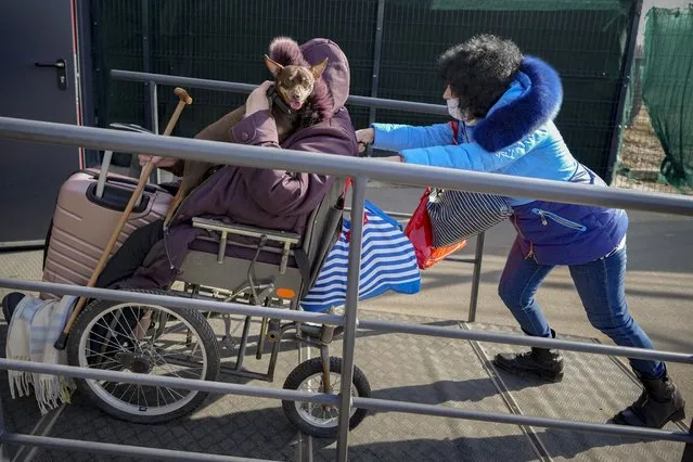 A woman pushes a wheelchair carrying an elderly woman holding a dog from pro-Russian separatists' controlled territory to Ukrainian government controlled areas in Stanytsia Luhanska, the only crossing point open daily, in the Luhansk region, eastern Ukraine, Tuesday, February 22, 2022. Russia says its recognition of independence for areas in eastern Ukraine extends to territory currently held by Ukrainian forces. The statement Tuesday further raises the stakes amid Western fears that Moscow could follow up to Monday’s recognition of rebel regions with a full-fledged invasion of Ukraine. (Photo by Vadim Ghirda/AP Photo)