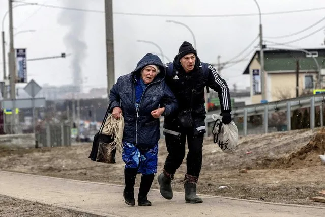 A man helps an elderly woman to run for cover after heavy shelling on the only escape route used by locals, while Russian troops advance towards the capital, in Irpin, near Kyiv, Ukraine on March 6, 2022. (Photo by Carlos Barria/Reuters)
