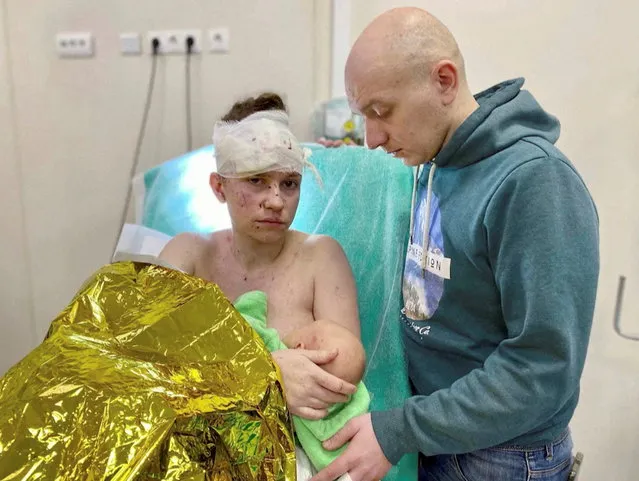 Olga, a 27-year-old Ukrainian woman seriously wounded while sheltering her baby from shrapnel blasts amid Russia's ongoing invasion of Ukraine, holds her baby Victoria as her husband Dmytro stands by her side in Kyiv, Ukraine, March 18, 2022, in this still image used in a video. (Photo by Okhmatdyt Children’s Hospital via Reuters TV)