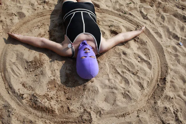 A woman, wearing a nylon mask, creates a circle in the sand as she lies down during her visit to a beach in Qingdao, Shandong province July 6, 2012. (Photo by Aly Song/Reuters)
