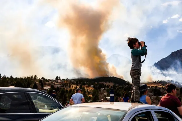 Amitai Beh, 6, watches the NCAR Fire through binoculars on March 26, 2022 in Boulder, Colorado. The wildfire, which has forced almost 20,000 people to evacuate their homes, started just a few miles away from where the Marshall Fire destroyed more than 1,000 homes in December, 2021. (Photo by Michael Ciaglo/Getty Images)