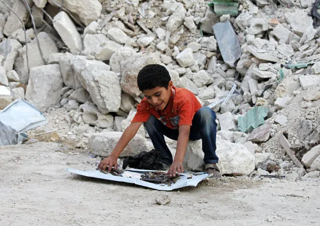 Ahmad, a Syrian boy, shows his collection of shrapnel and empty bullets in front of a destroyed house in Aleppo's Tariq al-Bab district September 12, 2012. Ahmad is collecting a piece from each shell that falls on his district and keeps them as souvenirs. (Photo by Zain Karam/Reuters)