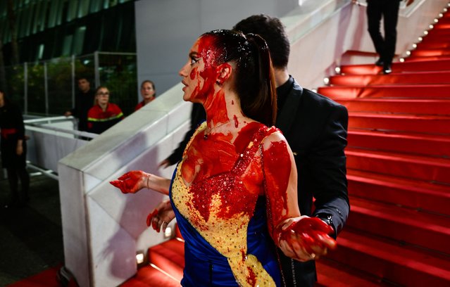 A protester, wearing a dress in the colours of the Ukrainian flag, is detained by security after she covered herself in fake blood on the stairs on the Festival Palace ahead of the screening of the film “Acide” during the 76th edition of the Cannes Film Festival in Cannes, southern France, on May 21, 2023. (Photo by Christophe Simon/AFP Photo)