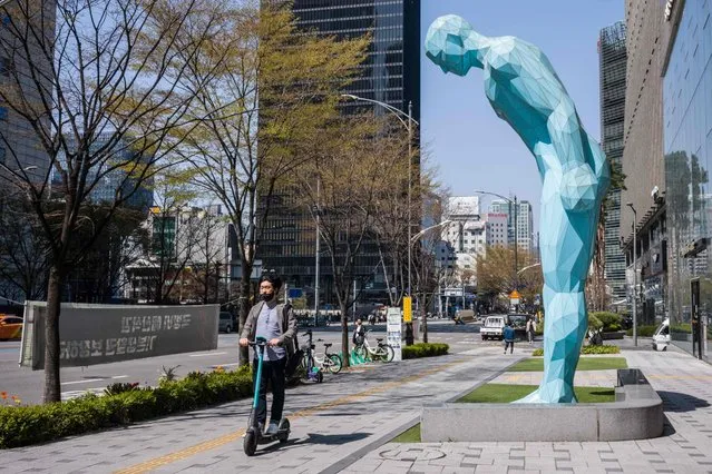 A man uses an electric scooter as he rides past a “Greeting Man” statue by South Korean artist Yoo Young-ho in Seoul on April 8, 2022. (Photo by Anthony Wallace/AFP Photo)