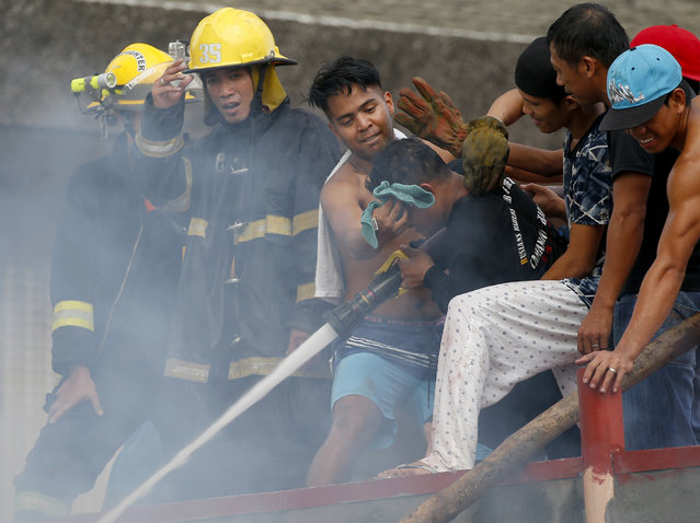 Informal settlers wipe the face of a fire volunteer as they help firemen in putting out a fire that swept through a poor neighborhood in suburban Pasay city southeast of Manila, Philippines Wednesday, June 21, 2017. Fire officials said no casualties were reported but the fire razed an undetermined number of houses and affected a few dozen families. (Photo by Bullit Marquez/AP Photo)