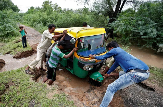 People try to push an auto-rickshaw stuck on a road damaged by flood water at a village on the outskirts of Ahmedabad, India, July 28, 2017. (Photo by Amit Dave/Reuters)