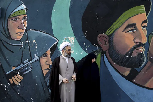 A cleric and his wife stand in front of a mural showing depicting members of paramilitary Basij during an annual pro-Palestinian rally marking Al-Quds (Jerusalem) Day in Tehran, Iran, Friday, June 23, 2017. Iran held rallies across the country, with protesters condemning Israel's occupation of Palestinian territories and chanting “Death to Israel”. (Photo by Ebrahim Noroozi/AP Photo)