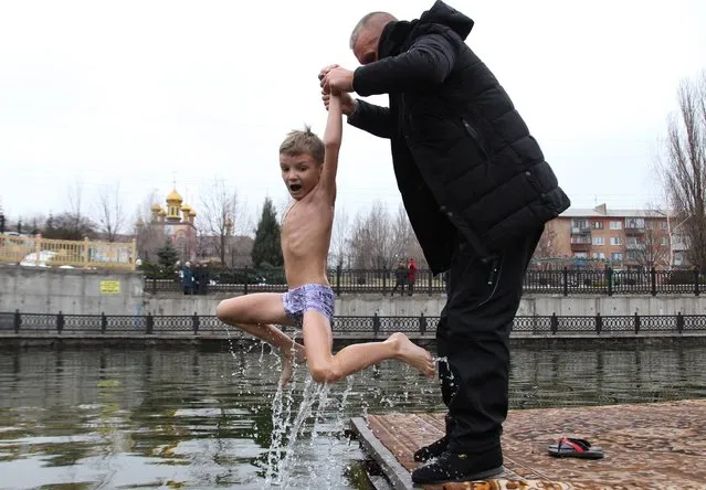 A man helps a child take a dip in a pond on the feast day of Epiphany, near St George's Church in Alchevsk, Lugansk Region, Ukraine on January 19, 2020. Orthodox Christians celebrate Epiphany according to the Julian calendar. (Photo by Alexander Reka/TASS)