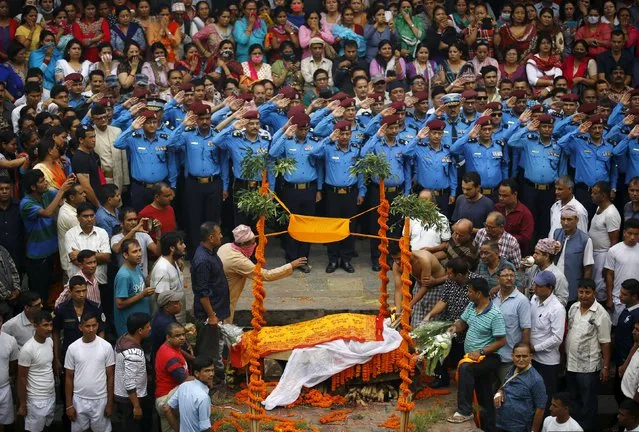 Nepali police officers salute as people watch the son (R) of Senior Superintendent of Police (SSP) Laxman Neupane cremate his father, who was killed in Monday's protest at Tikapur in Kailali district, in Kathmandu, Nepal August 25, 2015. Soldiers patrolled the small border town in Nepal's far west on Tuesday after nine people, most of them police, were killed in attacks by protesters angered by government reforms. (Photo by Navesh Chitrakar/Reuters)