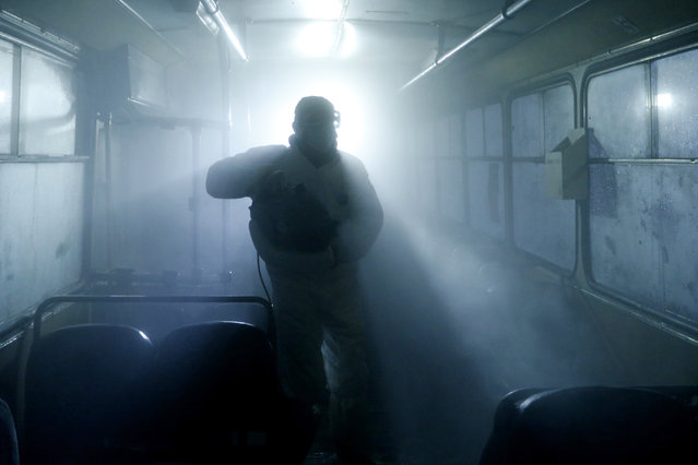 A man in protective gear disinfects a bus in Yerevan, Armenia on March 14, 2020. The disinfection consists of washing the exterior of a bus, dry sweeping and wet cleaning the inside and aerosol spraying. (Photo by Artur Harutyunyan/Yerevan City Administration/TASS)