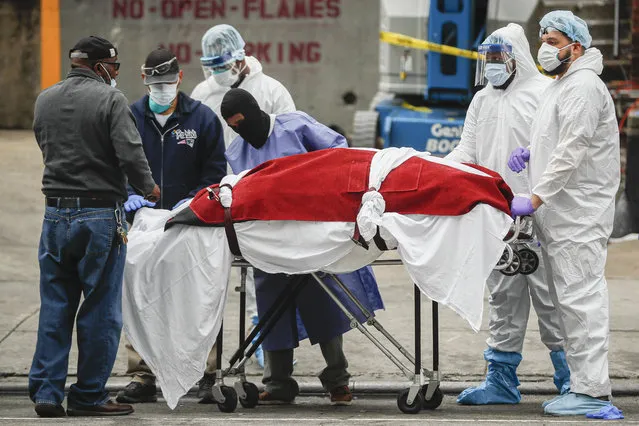 A body wrapped in plastic that was unloaded from a refrigerated truck is handled by medical workers wearing personal protective equipment due to COVID-19 concerns, Tuesday, March 31, 2020, at Brooklyn Hospital Center in Brooklyn borough of New York. The body was moved to a hearse to be removed to a mortuary. (Photo by John Minchillo/AP Photo)