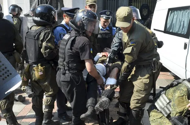 Ukrainian police and national guard officers carry an injured colleague to an ambulance outside the parliament building in Kiev, Ukraine, August 31, 2015. (Photo by Reuters/Stringer)