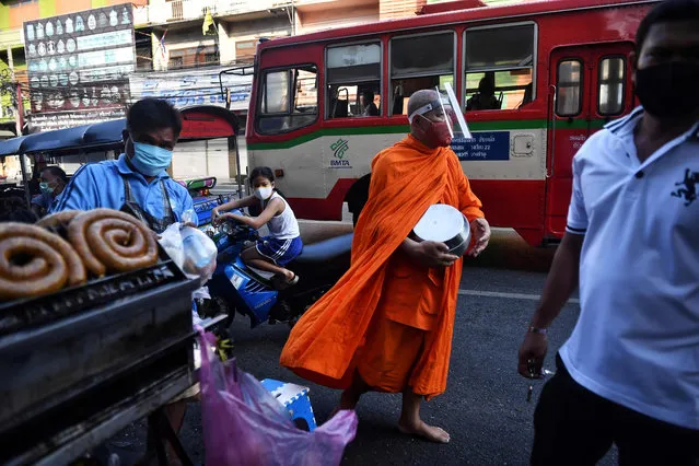A Buddhist monk collects alms while wearing a face shield, as a preventive measure against the spread of the COVID-19 novel coronavirus, at an outdoor market in Bangkok on April 17, 2020. (Photo by Lillian Suwanrumpha/AFP Photo)