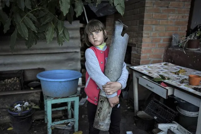Veronika Tkachenko, 7, holds a piece of a Grad rocket which hit her family's house in the recently retaken town of Izium, Ukraine, Sunday, September 25, 2022. (Photo by Evgeniy Maloletka/AP Photo)