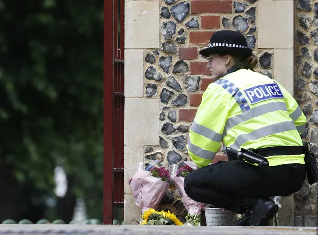 A police officer collects flowers left at the Abbey gateway of Forbury Gardens following a multiple stabbing attack which took place on Saturday, in Reading, England, Sunday June 21, 2020. Police say a stabbing rampage in Britain that killed three people as they sat in a park on a summer evening is being considered a terrorist attack. A 25-year-old man believed to be the lone attacker is in custody. (Photo by Alastair Grant/AP Photo)
