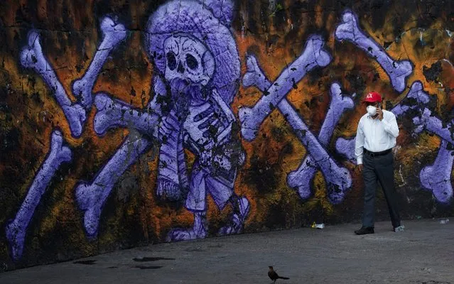 Arturo Morales, the coordinator of several public cemeteries, talks on his cell phone as he walks past a mural of a skeleton and bones that decorate the exterior of the Panteón San Nicolás Tolentino de Iztapalapa cemetery in Mexico City, Thursday, June 4, 2020. Funeral parlors and crematoriums in Iztapalapa, a borough of 2 million people, say they have seen their work multiplied with the surging number of dead of COVID-19 in the capital's hardest-hit corner by the new coronavirus. (Photo by Marco Ugarte/AP Photo)